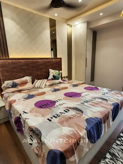 A comfortable bedroom with a dark wood-paneled accent wall and a plush brown headboard. The room opens up to a balcony, allowing for plenty of natural light.