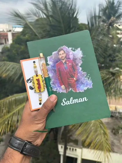 A personal and artistic Rakhi gift. This set includes a diary with a custom photo and name, a personalized pen, and a matching name rakhi made from MDF.