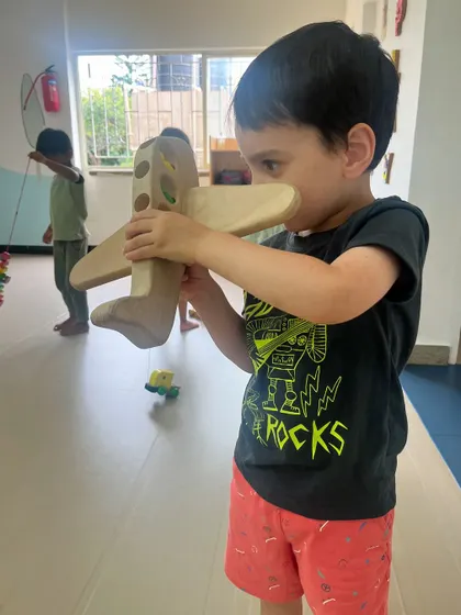 A young boy pretends to fly a large wooden airplane. Imaginative play with toys like this is often integrated with our building activities, inspiring new creations.