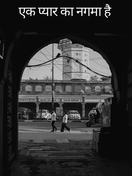 A beautifully framed black and white shot through an archway, capturing a candid moment of a couple walking through the streets of Jaipur, with the Hindi text "Ek pyar ka nagma hai" (A song of love).