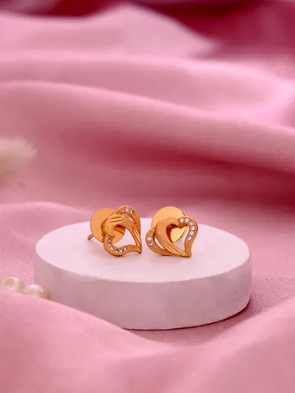 An elegant close up of heart shaped gold earrings on a white podium. The soft pink background and delicate pearls create a romantic and gentle mood, perfect for showcasing gift items.