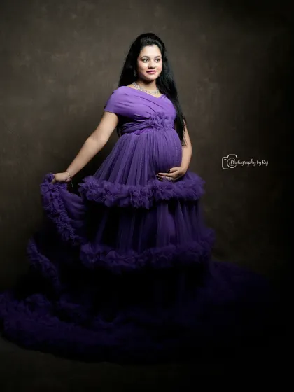 A beautiful studio portrait of a mother-to-be in a purple ruffled gown, with the dress flowing elegantly.