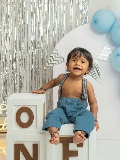 The pure joy of turning one. This little boy's infectious laugh is the highlight of this clean and bright birthday setup, complete with a silver tinsel backdrop and blue balloons.