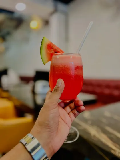 A hand-held shot of a fresh watermelon juice. This personal perspective makes the drink feel more immediate and refreshing, as if you're about to take a sip yourself.