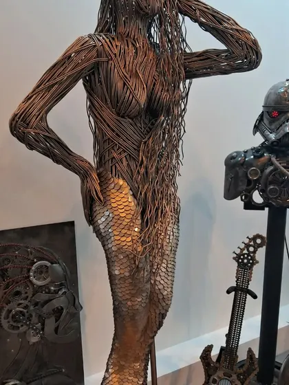 A striking metal sculpture of a mermaid, with her hair and torso woven from wires and her tail made of scaled plates.