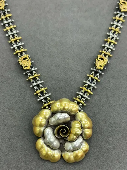 This dual-tone necklace showcases a modern floral design. The pendant features layered gold and silver petals with a spiral centre, attached to a unique chain of alternating silver and gold-plated links.