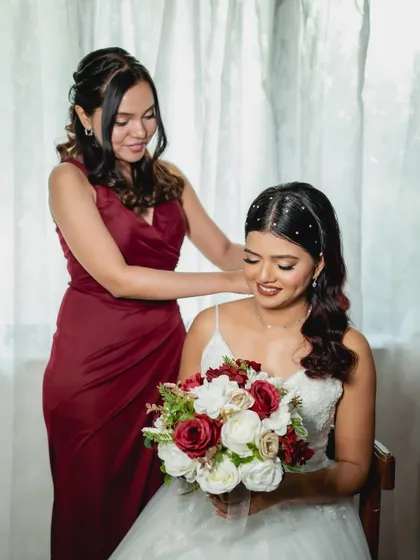 A sweet moment between the bride and her bridesmaid. Her hair is styled with delicate pearl accessories, and her makeup is soft and romantic.