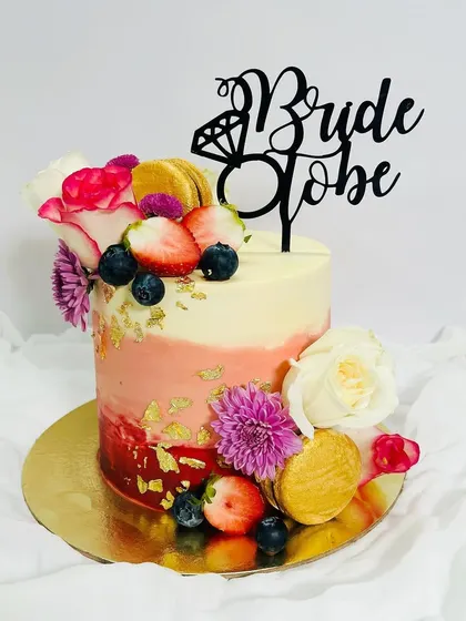 A stunning cake for a bride-to-be. This tall, single-tier cake features a red and pink ombre effect, and is lavishly decorated with fresh berries, flowers, and macarons.