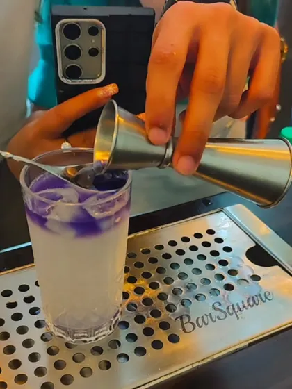 A close-up of a layered cocktail being prepared. This technique creates a beautiful visual effect, with a purple layer floating on top of a milky white base, demonstrating precision and artistry.