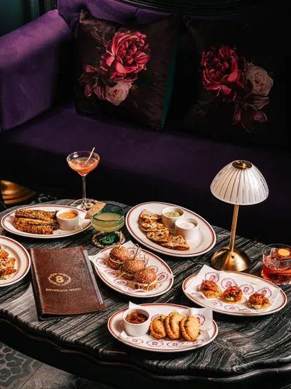 A lavish spread of food and cocktails at Ocho Bandra, set against a plush purple sofa. This shot communicates a sense of opulence and indulgence.