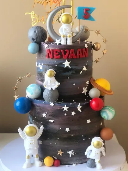 A two-tiered galaxy cake with astronauts, planets, and stars, perfect for a space-themed party.