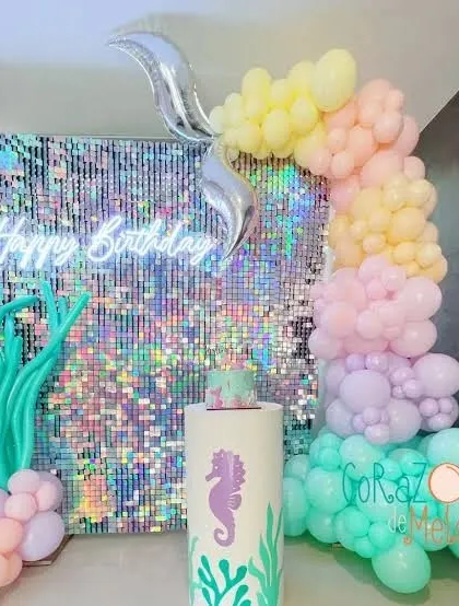 A mermaid-themed birthday with an iridescent shimmer wall, a 'Happy Birthday' neon sign, and a pastel balloon garland.