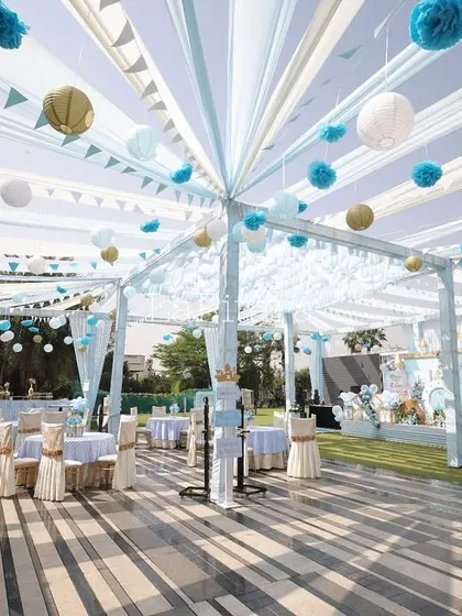 An expansive outdoor tented area for a royal celebration, with flowing white and blue drapes creating a dreamy canopy. The space is elegantly set with coordinated tables and chairs, ready to host guests in style.