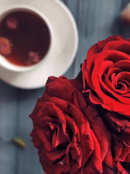 A close-up shot focusing on the deep red petals of a rose, with a cup of tea blurred in the background. This image is less about the food and more about creating a mood of love and beauty.