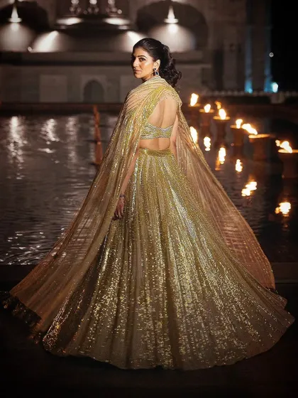 A full-length view of the bride's stunning golden gown with a dramatic cape, showcasing a modern and high-fashion choice for a sangeet or cocktail event.