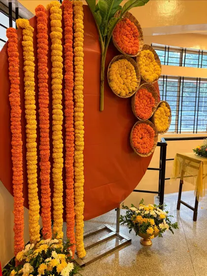 A unique and modern Haldi backdrop. This design features a large circular panel decorated with hanging marigold garlands and baskets filled with fresh flowers.
