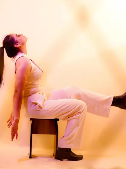 An artistic pose, using the stool as a prop. The warm lighting creates a dramatic and abstract feel.