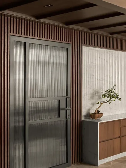 A detail of the entrance at Project Acropolis. A custom metal and fluted glass door provides security while allowing light to pass through, set against a backdrop of fluted wood and marble.