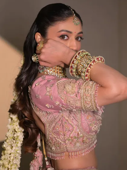 A playful and confident pose. The makeup is flawless, and the soft pink tones complement her beautiful pastel lehenga.