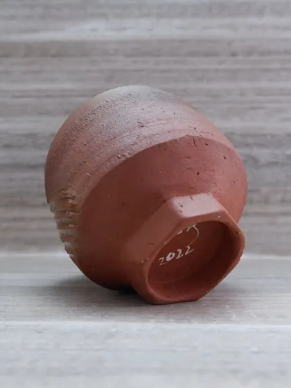 The bottom of a handmade earthenware tea bowl, showing my signature and the year it was made. The unglazed foot reveals the raw, warm color of the clay itself.