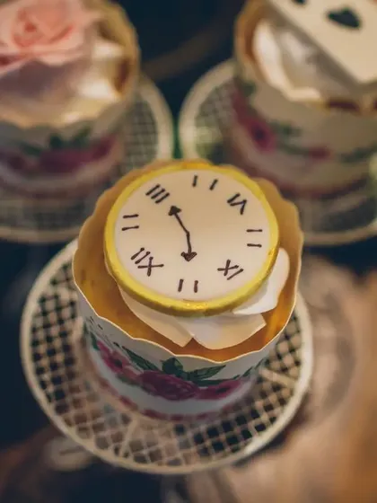 A close-up of a whimsical cupcake topped with a fondant clock, capturing the "I'm late!" essence of the White Rabbit. Every dessert is a tiny, edible piece of the story.