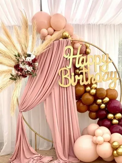 A bohemian-chic birthday setup with a gold ring, pampas grass, and a balloon garland in earthy tones. The custom 'Happy Birthday' sign adds a personal touch.