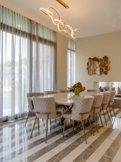 Dine in style in this peaceful dining area where grey meets beige. The striped marble floor, quilted chairs with gold-finished legs, and a modern light fixture create a perfect recipe of minimalism and warmth.
