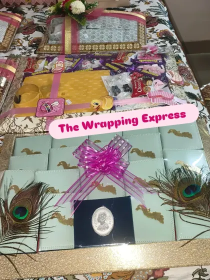A complete baby girl trousseau display, including packed cash gift envelopes with peacock feathers and a hamper of chocolates and clothes.