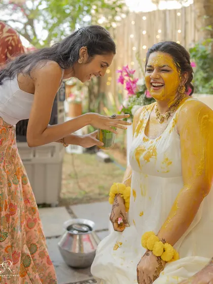 A friend joins in on the fun, applying haldi to the bride during the ceremony.