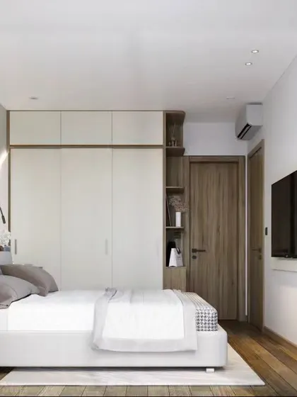 A minimalist bedroom featuring a clean, all-white color scheme with natural wood flooring. The design includes a simple platform bed and a large wardrobe, creating a bright and airy space that feels open and uncluttered.