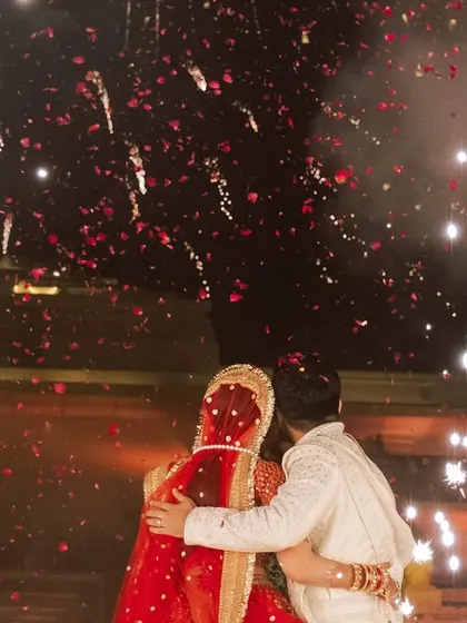 A beautiful, candid moment of the couple embracing during their varmala ceremony, framed by a shower of rose petals and fireworks. These are the emotional peaks I aim to create.