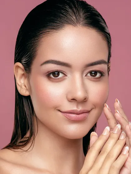 A clean, fresh-faced portrait against a soft pink background. The wet-look hair and minimal makeup emphasize a 'just out of the shower' feeling, focusing entirely on the model's naturally beautiful and well-hydrated skin.