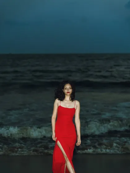A full-length shot showing the elegant red dress against the vast, dark ocean. It's a very dramatic and lonely, yet powerful, scene.