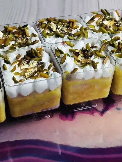 A side view of the Kesar Pista Tres Leches Cups, showing the layers of saffron-soaked cake and fluffy white cream, topped with pistachios.