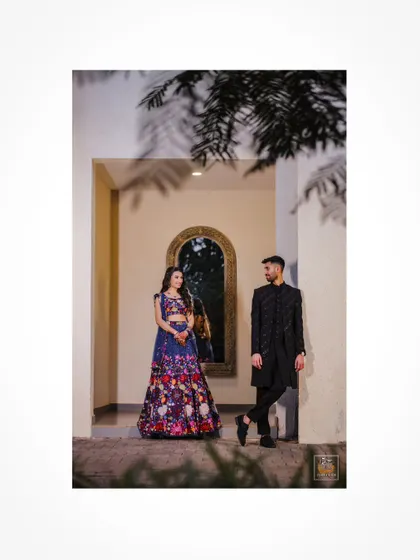 A full-length shot of the couple, showcasing their floral and classic black Sangeet attire.