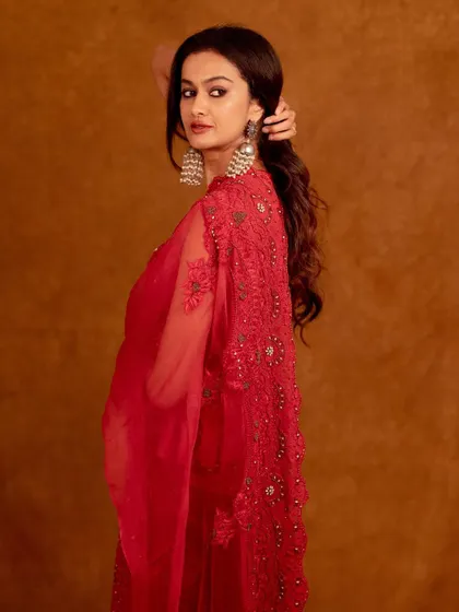 A three-quarter shot showing the full sweep of the red dupatta. The pose is graceful and powerful.