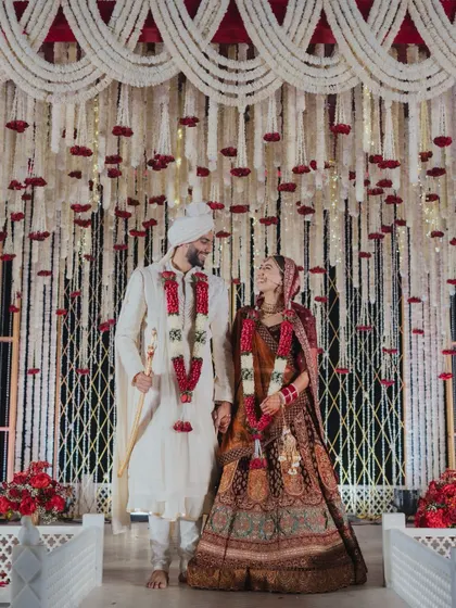 Another beautiful shot of the couple, framed by the intricate floral mandap. The lighting and decor work together to create a warm, celebratory atmosphere.