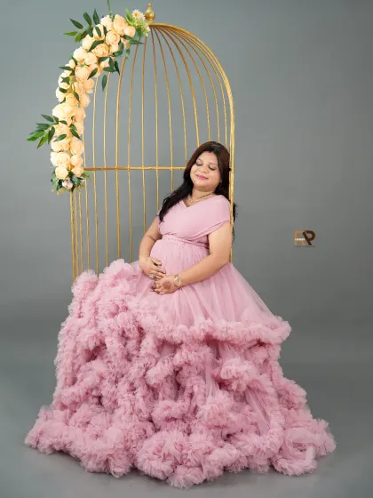 A serene moment of reflection. The mom-to-be sits peacefully in our golden birdcage prop, cradling her bump in a voluminous pink ruffled gown.