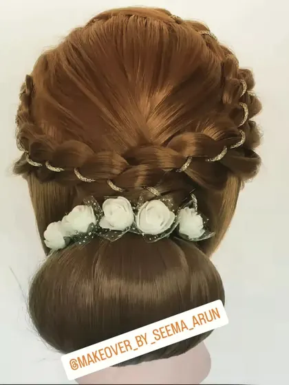 This classic bun is elevated with a crown of braids, interwoven with a fine gold thread. A line of small white flowers at the base adds a soft, traditional touch, making it suitable for both muhurtham and party looks.