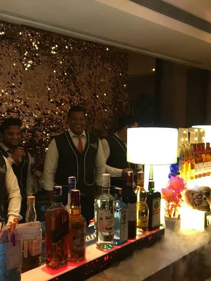 Our smiling team of bartenders and butlers, ready to serve at a glamorous event with a sequin backdrop.