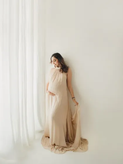 A full length portrait showcasing this gorgeous, flowing beige gown against a clean white backdrop. The simplicity of the setting makes the mother to be the complete focus.