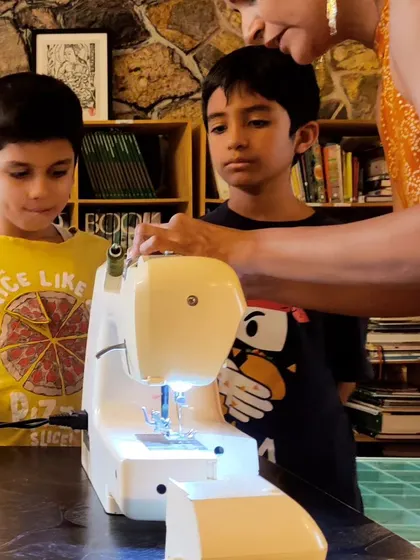 Two boys receive a lesson on the sewing machine. We believe in trusting children with real tools, and they learn to use them with respect, care, and intense focus.