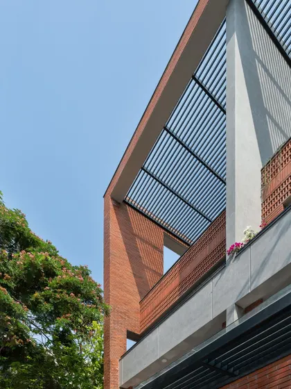 This apartment facade features a combination of exposed brick and a slatted pergola roof. These elements frame the sky and create dynamic shadows, adding texture and depth to the building's exterior.