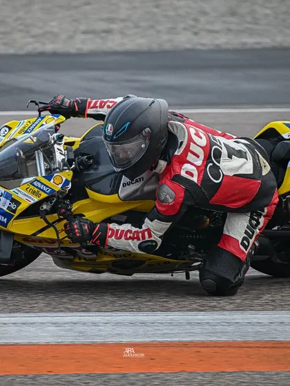 A yellow Ducati captured mid-corner, demonstrating the rider's excellent body positioning and focus. Every detail, from the gear to the bike's angle, tells a story of speed.
