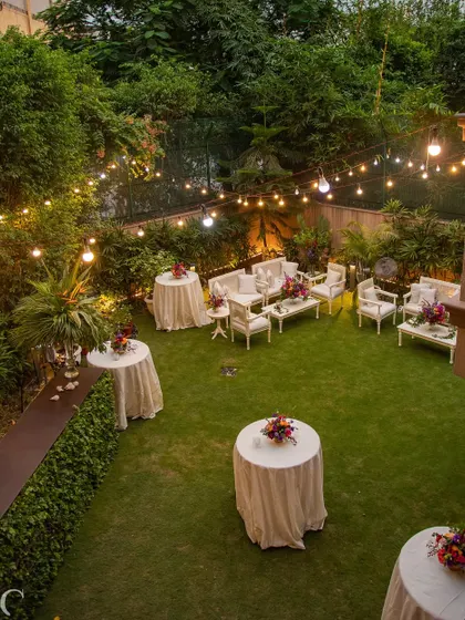 An aerial view of an intimate garden soirée, with string lights creating a magical canopy over the lawn. The white lounge furniture and cocktail tables are arranged to encourage conversation and mingling.
