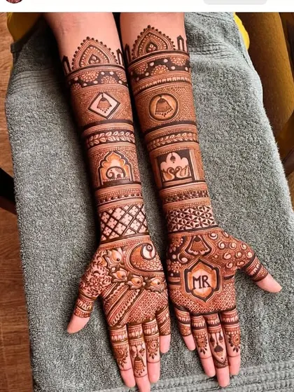 An elegant engagement mehandi with personalized initials. The design is a mix of traditional symbols like the lotus and bell with modern geometric patterns.