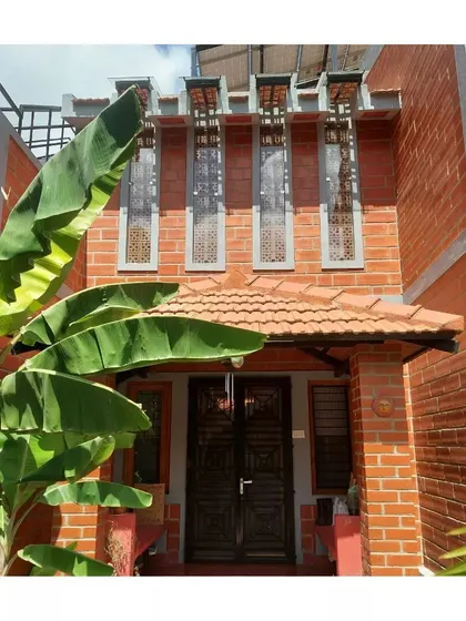 The entrance to the Anjali and Anshuman residence, where a banana plant frames the view of the exposed brick facade and decorative jaali windows.