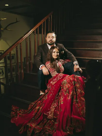 A stunning portrait of the couple on the stairs. The bride's red anarkali drapes beautifully, creating a regal and elegant silhouette.