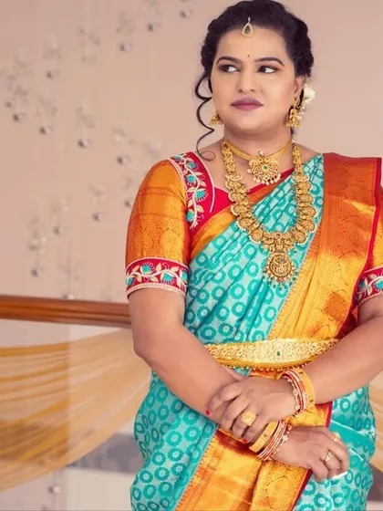 A solo portrait showcasing the traditional look. The turquoise and orange saree is complemented by a soft smokey eye and a neutral lip.