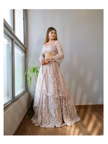 A portrait of a bride in a beautiful lavender lehenga, looking elegant by a window.